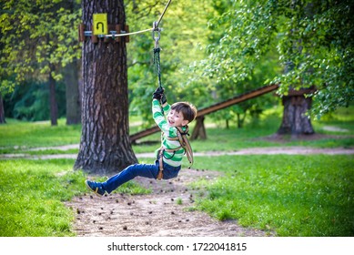 Smiling Boy Rides A Zip Line. Happy Child On The Zip Line. The Kid Passes The Rope Obstacle Course.