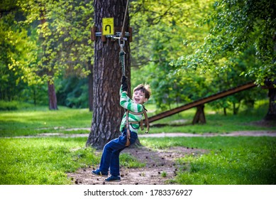 Smiling Boy Rides A Zip Line. Happy Child On The Zip Line. The Kid Passes The Rope Obstacle Course.