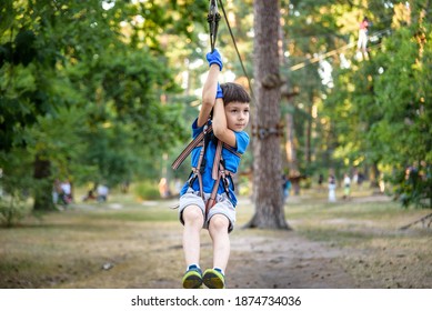 Smiling Boy Rides A Zip Line. Happy Child On The Zip Line. The Kid Passes The Rope Obstacle Course.