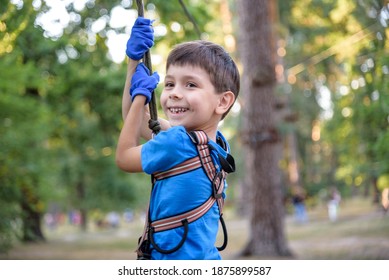 Smiling Boy Rides A Zip Line. Happy Child On The Zip Line. The Kid Passes The Rope Obstacle Course.