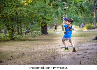 Smiling Boy Rides A Zip Line. Happy Child On The Zip Line. The Kid Passes The Rope Obstacle Course.