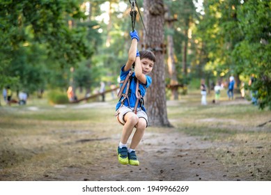 Smiling Boy Rides A Zip Line. Happy Child On The Zip Line. The Kid Passes The Rope Obstacle Course.