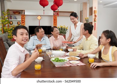Smiling boy sitting at dinner table for Vietnamese New Year celebration; couplets with best wishes for coming year in the background