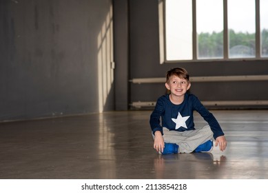 Smiling Boy Sitting On The Floor In An Empty Dance Hall