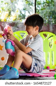 smiling boy sitting sideways playing with a doll
