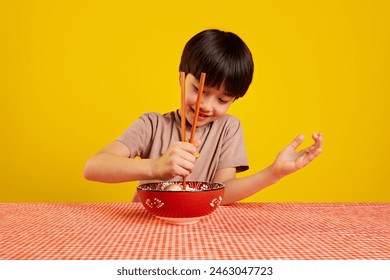 Smiling boy sitting at table and with plate of ramen soup and learning to eat with chopsticks against yellow background. Concept of food, childhood, emotions, Japanese meal, menu, pop art - Powered by Shutterstock