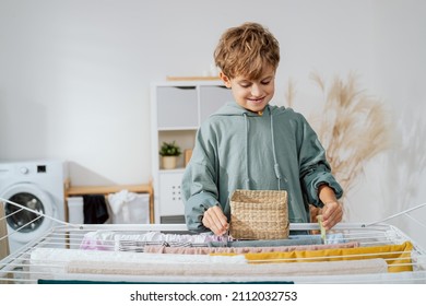 Smiling boy spends time in bathroom, laundry room placing clips on already washed clothes hanging on dryer, helping with household chores - Powered by Shutterstock