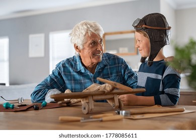 Smiling boy wearing pilot hat and helping making wooden airplane with his grandpa. Happy grandson helping old grandfather making wooden airplane. Playful child wearing aviator helmet enjoying. - Powered by Shutterstock