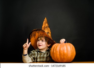 Smiling boy in witch hat with halloween pumpkin. Kid with pumpkin. Halloween holidays. Trick or treat. Halloween boy pointing finger up. Halloween costume. Funny Pumpkin. Celebration party. 31October.