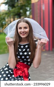 Smiling Bride In A Veil And Black Dress In White Apple With A Red Sash .