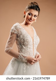 Smiling bride in white wedding dress with deep decollete smiling and looking in camera. Lace bridal gown with transparent long sleeves, front slit, tulle skirt and floral embroidery. Happy marriage.