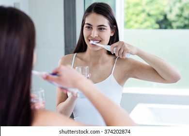 Smiling brunette brushing teeth in bathroom