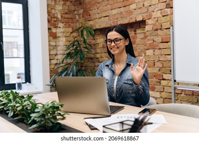 Smiling Brunette Business Woman Waving Hello To Coworkers On Laptop Screen During Online Meeting In Office Room