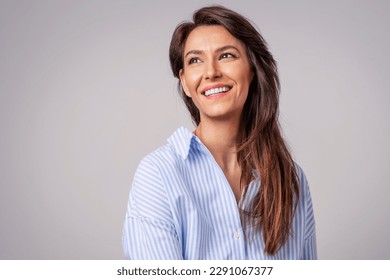 Smiling brunette businesswoman sitting against gray background. Confident female professional is wearing blue shirt. She is having brown hair. Copy space. - Shutterstock ID 2291067377