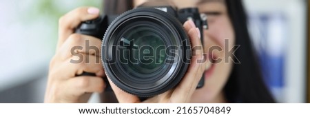 Smiling brunette female photographer pointing super wide lens at you