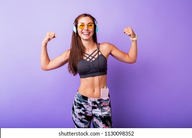 Smiling brunette  sporty woman showing muscles  and smiling. Perfect athletic body. Purple background. 