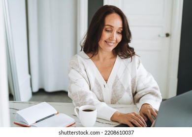 Smiling Brunette Woman With Long Hair In White Cardigan Working On Laptop In Bright Modern Office