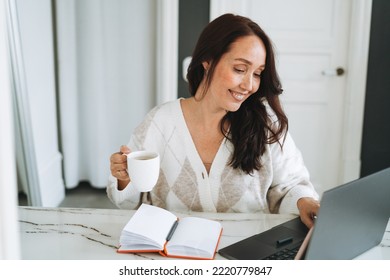 Smiling Brunette Woman With Long Hair In White Cardigan Working On Laptop In Bright Modern Office