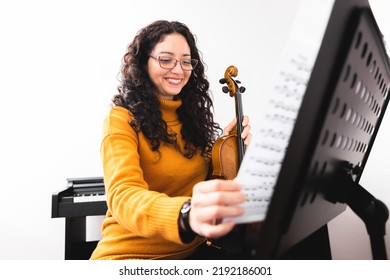 Smiling Brunette Woman Wearing A Yellow Sweater, Playing Violin And Turning De Page Of Sheet Music.