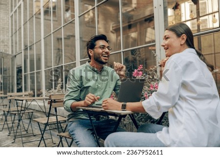 Smiling business colleagues discuss biz issue while use laptop sitting in office terrace