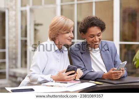 Smiling business colleagues discuss biz issue while use mobile phones sitting in office terrace