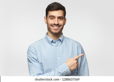 Smiling Business Man Pointing Right With Index Finger And Looking At Camera, Isolated On Gray Background