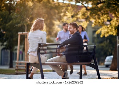 Smiling business man and woman sitting at bench at park and talking.