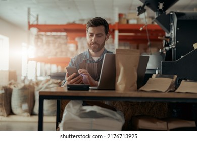 Smiling Business Owner Of Small Coffee Roasting Factory Working On Workplace With Laptop And Phone