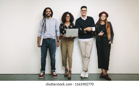 Smiling Business People Holding Laptops And Digital Tablet Standing Against A Wall In Office. Businessman Relaxing Holding A Cup Of Coffee Standing With His Colleagues In Office.