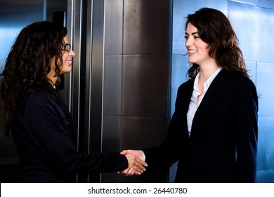 Smiling Business People Shaking Hands At Office Lobby In Front Of Elevator.