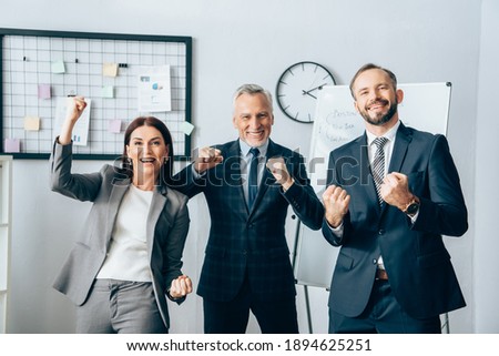 Smiling business people showing yeah gesture at camera near flipchart in office