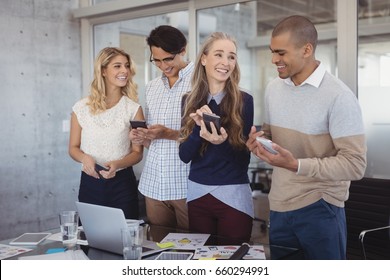 Smiling Business People Using Mobile Phones In Creative Office