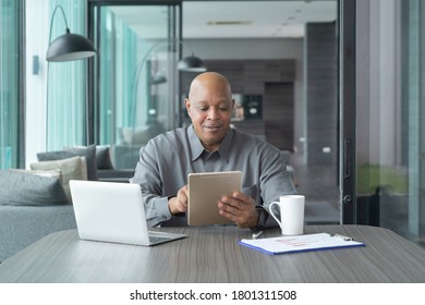 Smiling Business Senior Old Elderly Black American Man, African Person Working From Home On Table With Tablet And Notebook Computer Laptop In Quarantine In Corona Virus Pandemic Concept.