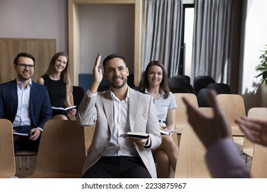 Smiling business training participant raising hand asking speaker, coach or mentor having question at meeting or educational seminar in boardroom with teammates. Man voting as volunteer at workshop