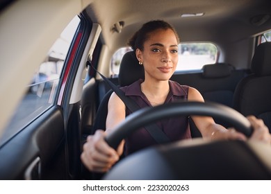 Smiling business woman driving car in city streets. Happy african american woman feeling comfortable sitting on driver seat in her new car. Mixed race girl with seat belt driving vehicle.