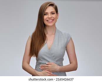 Smiling Business Woman Has Her Hands On Her Stomach. Isolated Portrait Of Beautiful Girl With Long Hair Wearing Gray Business Dress.