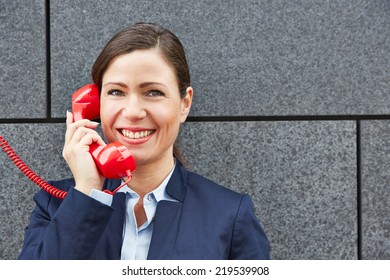 Smiling Business Woman Making Call With Red Phone And Leaning On A Wall