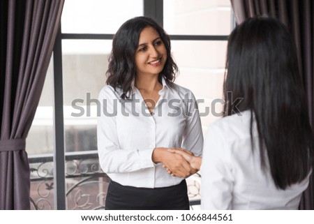 Smiling business woman shaking hands with partner at cafe window. Other woman is unrecognizable. Deal concept.