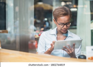 Smiling business woman using digital tablet behind large glass window
