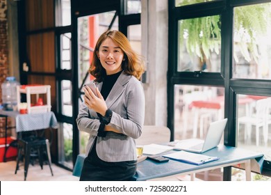 Smiling Business woman working in office with documents,Happy Asian businesswoman using phone sitting on chair at modern home studio.Concept of young people working mobile devices,contact to costumer - Powered by Shutterstock