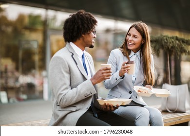 Smiling businessman and businesswoman with sandwiches sitting in front of the office building - lunch break - Powered by Shutterstock