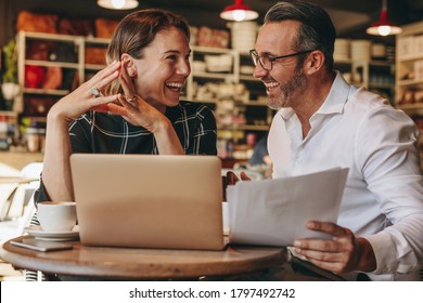 Smiling Businessman And Businesswoman Sitting At Coffee Shop With Laptop And Documents. Business People Working At Coffee Shop.