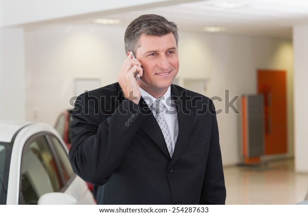 Smiling businessman calling with his mobile\
phone at new car\
showroom