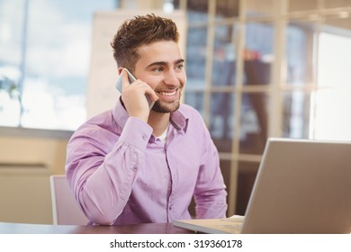 Smiling businessman calling on phone while working in office - Powered by Shutterstock