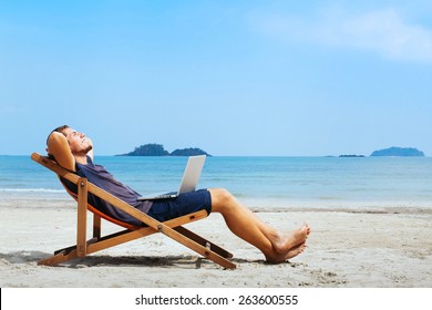 smiling businessman with computer relaxing on the beach - Shutterstock ID 263600555