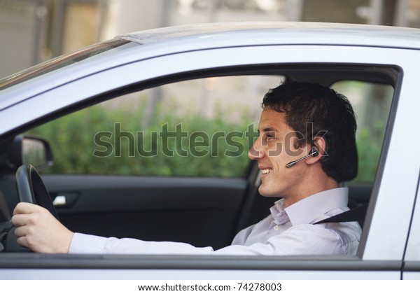 Smiling businessman driving a car with\
blue-tooth hands-free