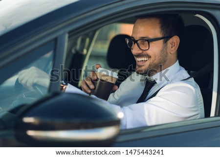Smiling businessman driving a car while drinking coffee