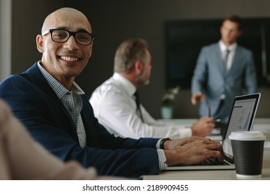 Smiling Businessman During A Meeting In Conference Room. Male Executive Sitting On Office Board Room With Colleagues Discussing In Background.