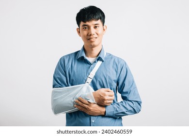 Smiling businessman endures broken arm and associated discomfort, using treatment splint. An excited Asian man with arm sling isolated on white background, illustrating recovery process. Copy space
