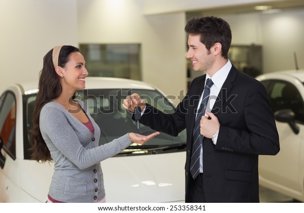 Smiling businessman giving car key to happy\
customer at new car\
showroom
